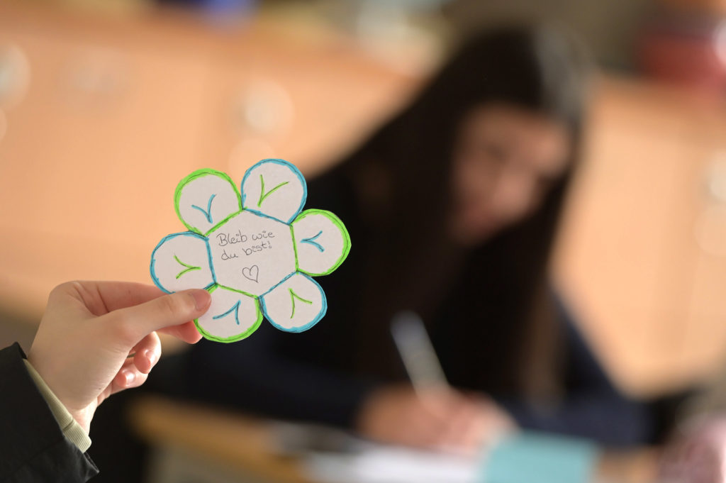 Eine ausgeschnittene Blume, auf der handschriftlich zu lesen ist: "Bleib, wie du bist!"