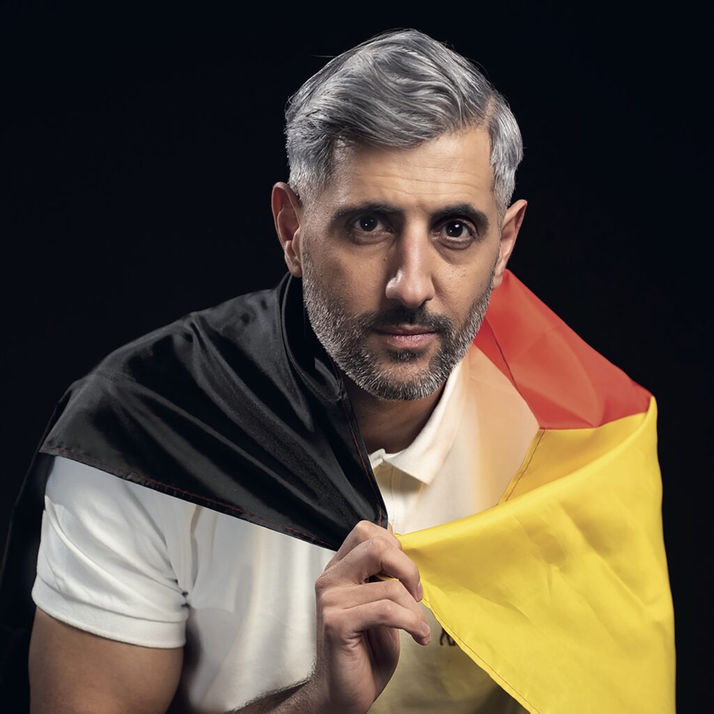 Porträtfoto von Michel Abdollahi, der eine Deutschlandfahne wie einen Umhang trägt.